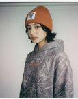 Person wearing a patterned hoodie and orange beanie against a plain background