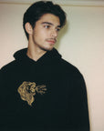 Person wearing a black hoodie with a gold lion design on a plain background