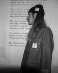 Person wearing a jacket with a patch in front of a wooden wall with text.