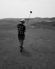 Person walking on a golf course with a golf club, black and white photo
