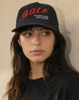 A woman wearing a black baseball cap with red and white embroidered text that reads 'G.O.L.F.