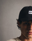 Person wearing a black cap with a visible brand logo against a plain background