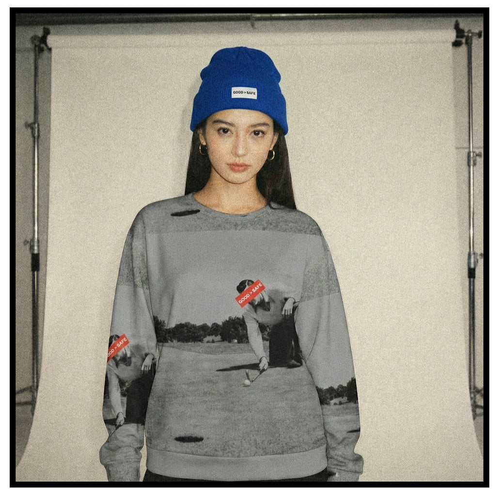 Person wearing a gray sweatshirt with graphic designs and a blue beanie indoors.