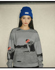 Person wearing a gray sweatshirt with graphic designs and a blue beanie indoors.