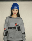 Person wearing a gray sweatshirt with a graphic design and a blue beanie indoors.