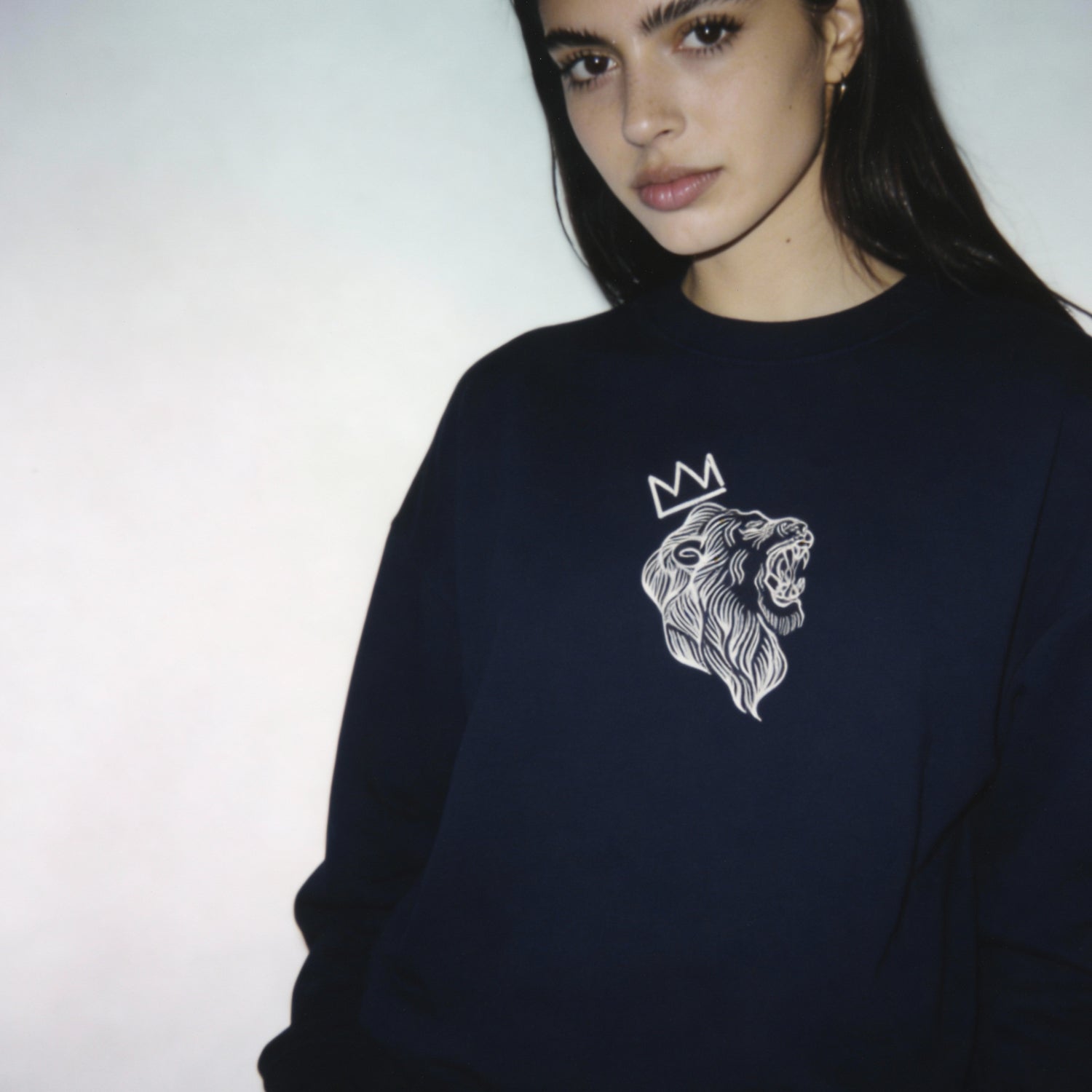 Person wearing a navy sweatshirt with a lion emblem and crown design on a plain background