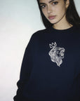 Person wearing a navy sweatshirt with a lion emblem and crown design on a plain background