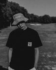 Person wearing a black t-shirt with a logo and a bucket hat on a golf course.