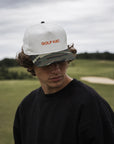 Person wearing a white cap with 'GOLF HAT.' text on a golf course