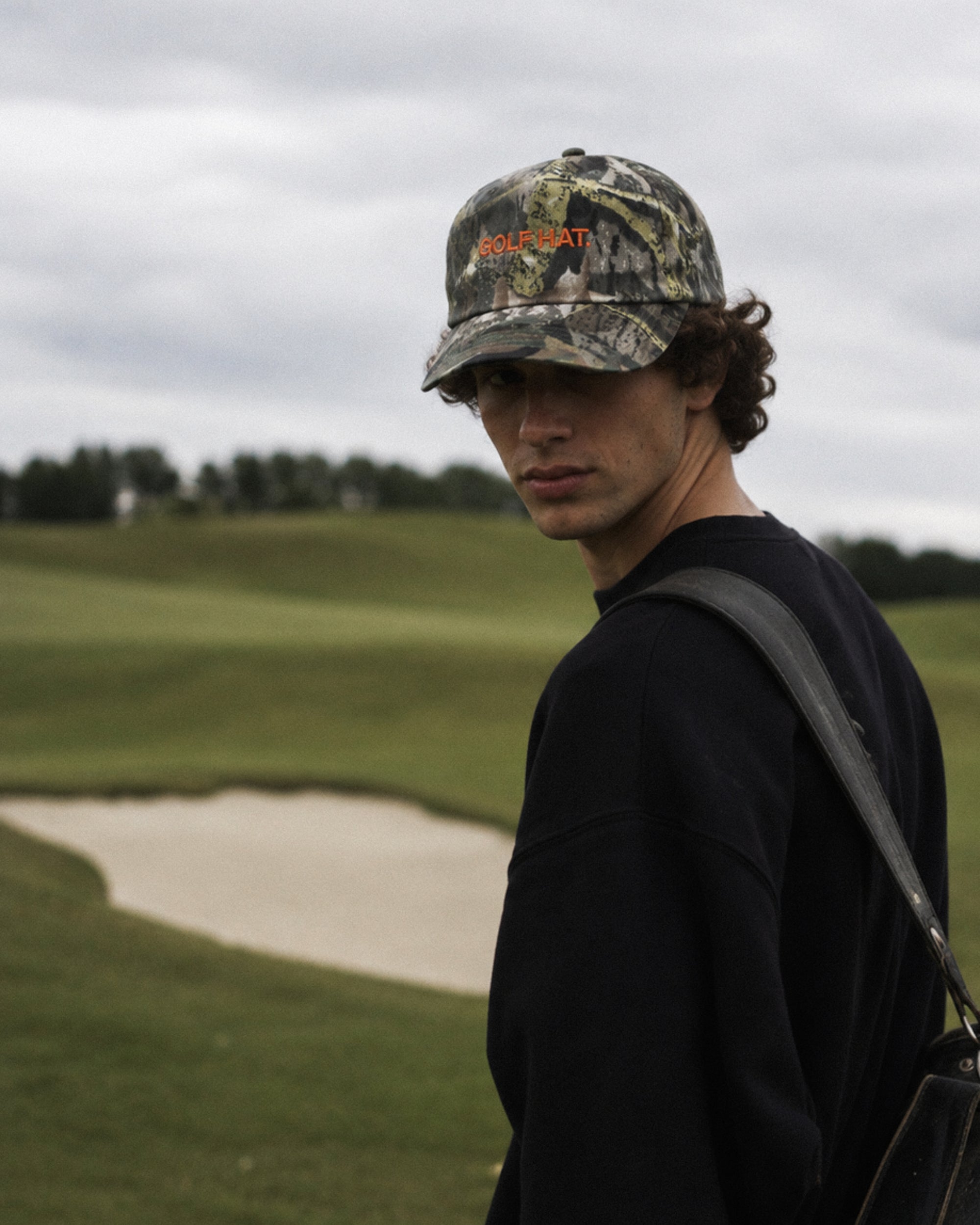 Person wearing a camouflage cap and black shirt on a golf course