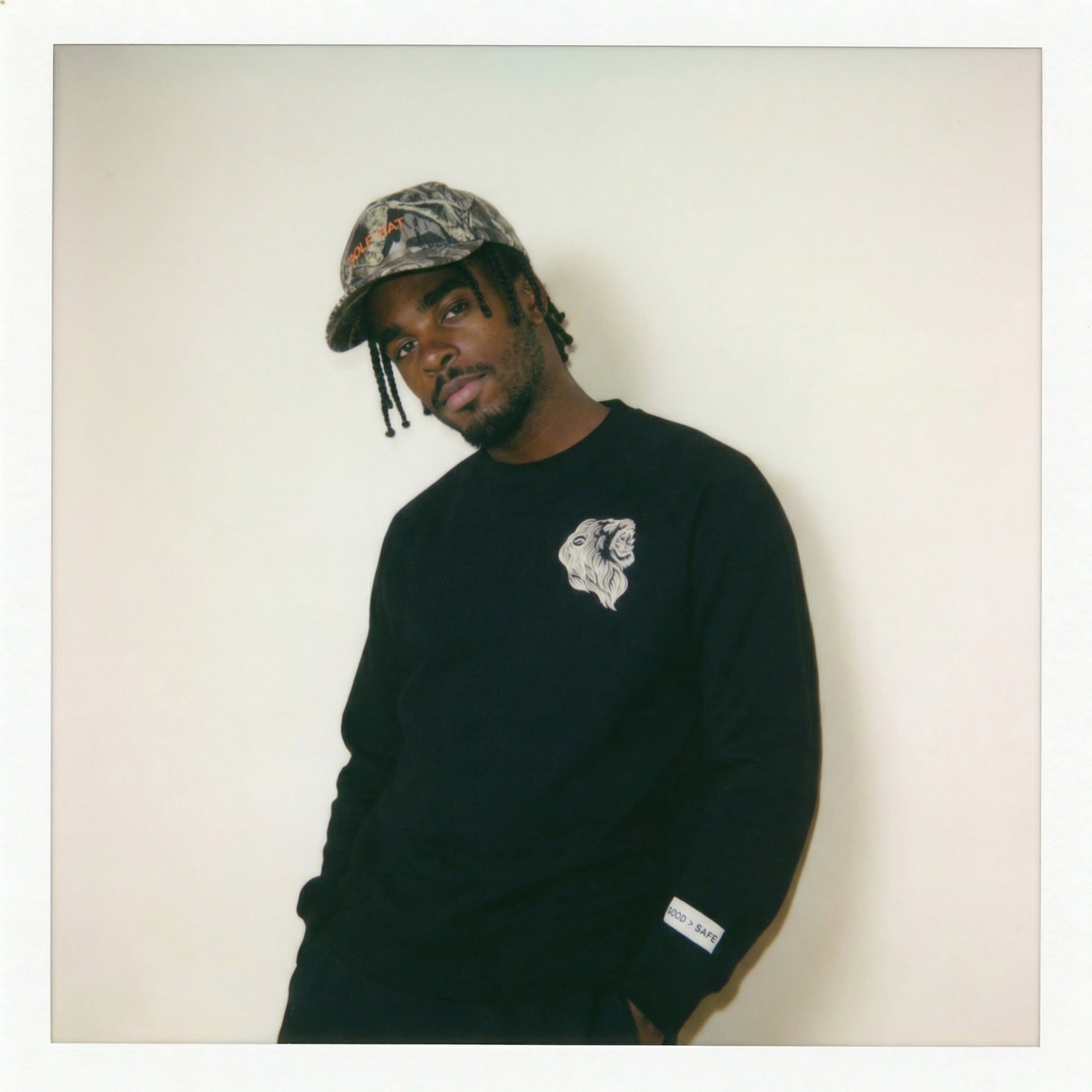 Person wearing a black sweatshirt with a logo and a camouflage cap against a plain background