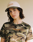 Person wearing a camouflage t-shirt and cap with 'GOLF' branding on a plain background