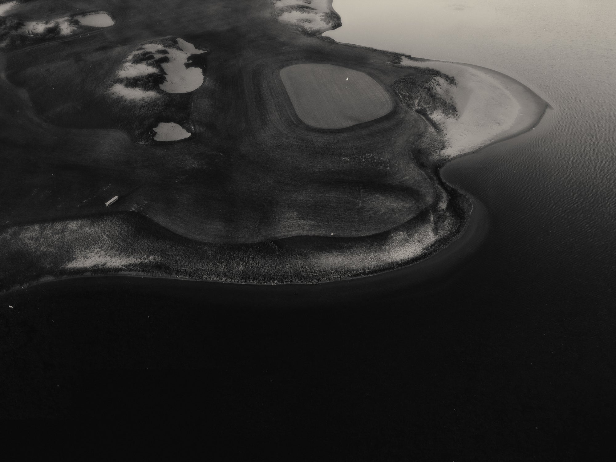 Black and white photo of a small island with a lighthouse in the middle of a body of water.