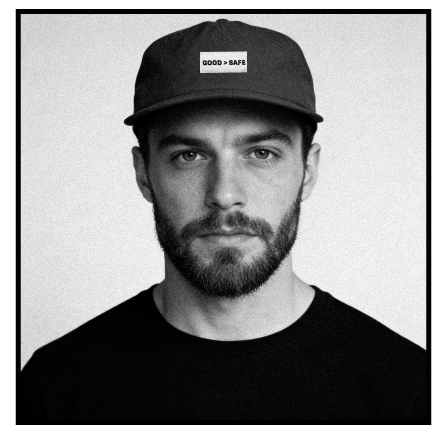 Man wearing a cap with 'GOOD > SAFE' text on a plain background