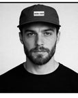 Man wearing a cap with 'GOOD > SAFE' text on a plain background