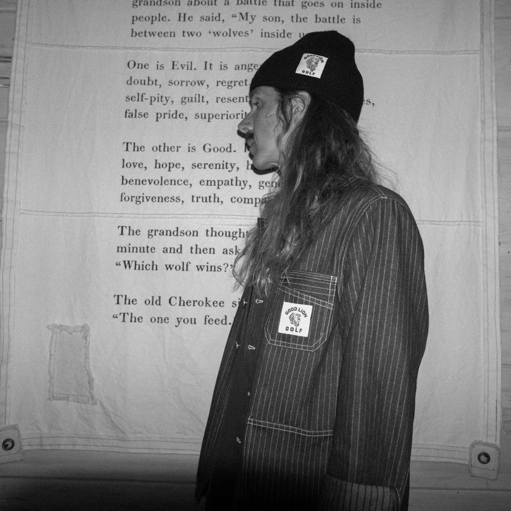 Person wearing a jacket with a patch in front of a wooden wall with text.