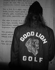 Person wearing a jacket with 'Good Lion Golf' logo in front of a wooden wall with text.