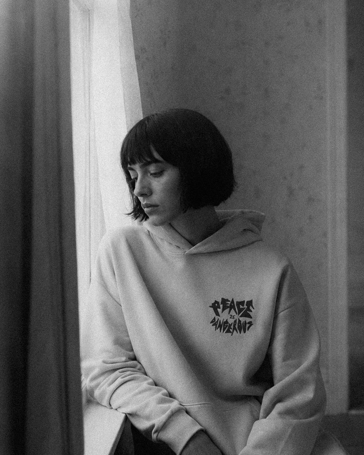 Person wearing a hoodie with text, sitting by a window.