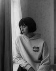 Person wearing a hoodie with text, sitting by a window.