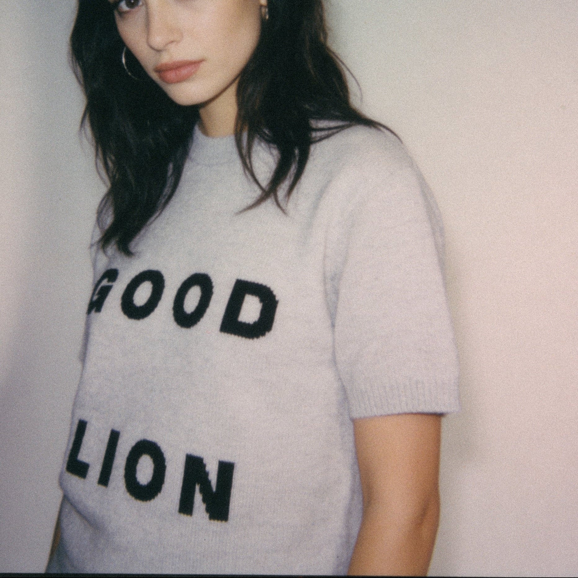 Person wearing a gray sweater with 'GOOD LION' text on a plain background