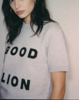 Person wearing a gray sweater with 'GOOD LION' text on a plain background
