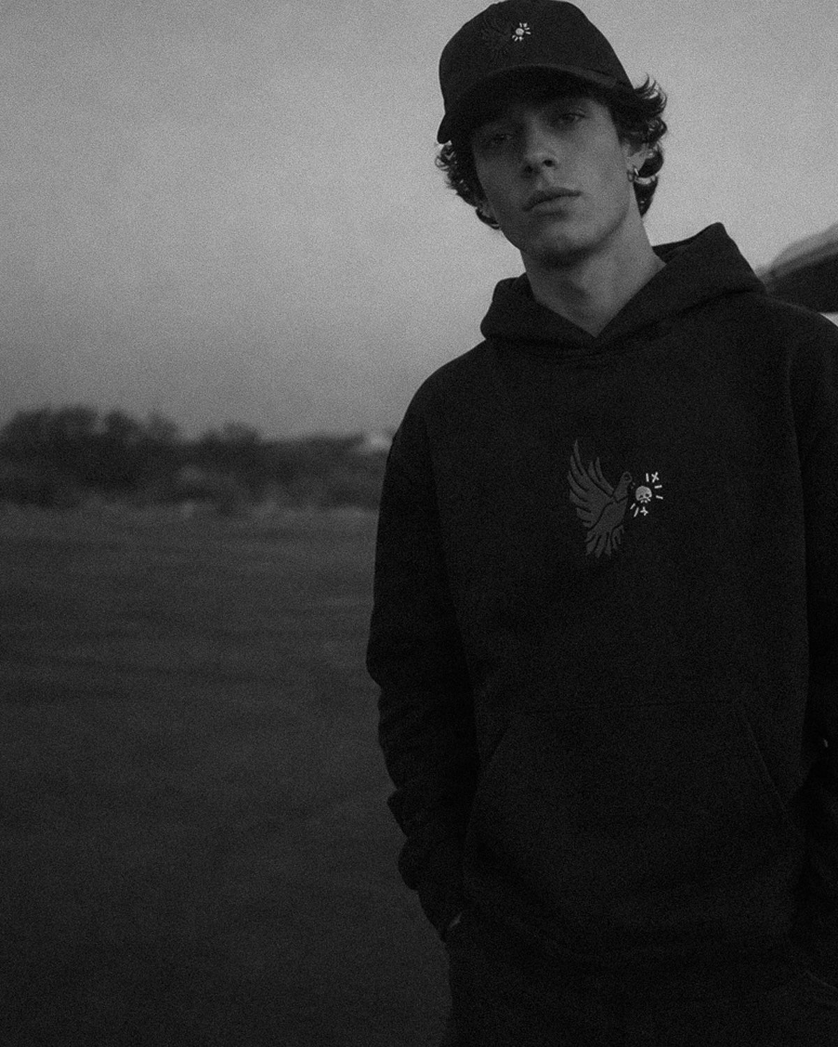 Person wearing a black hoodie with a logo in a field at dusk