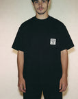 Person wearing a black t-shirt with a small white logo on a plain background