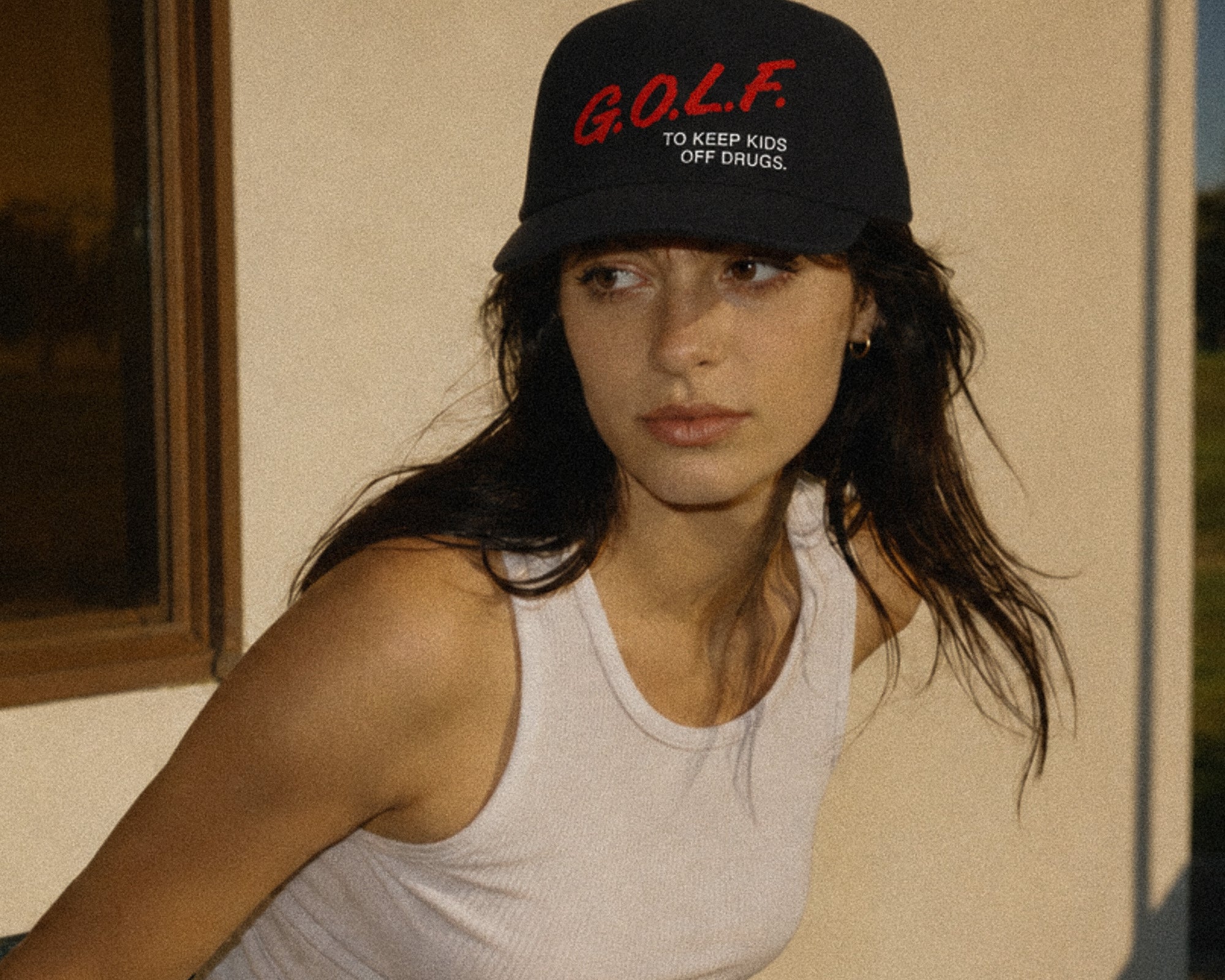 A woman wearing a black baseball cap with red and white embroidered text reading 'G.O.L.F.'