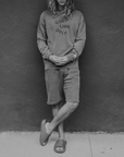 Person wearing a 'Good Lion' sweatshirt and shorts against a dark wall.
