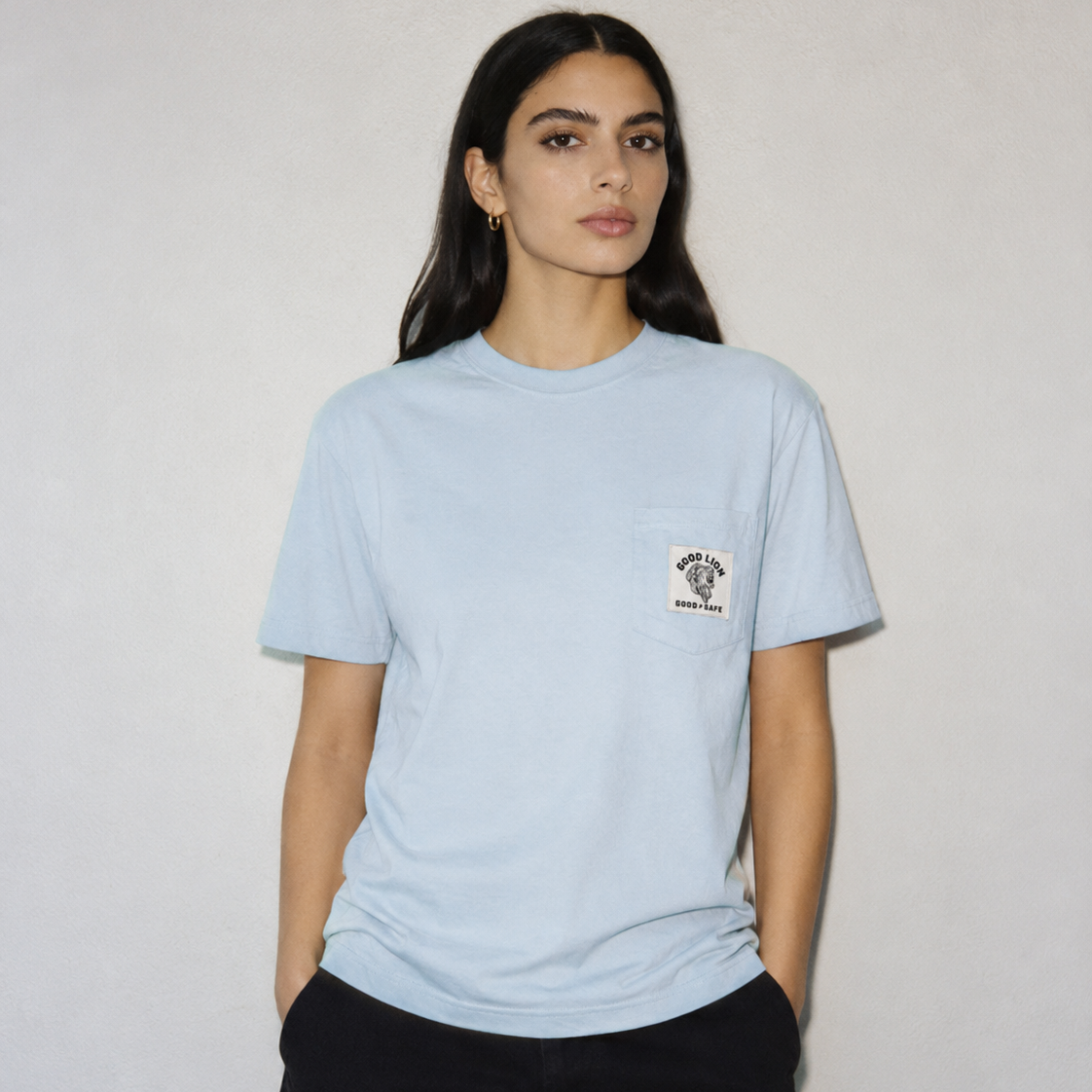 Woman wearing a light blue t-shirt with a small logo on a plain background