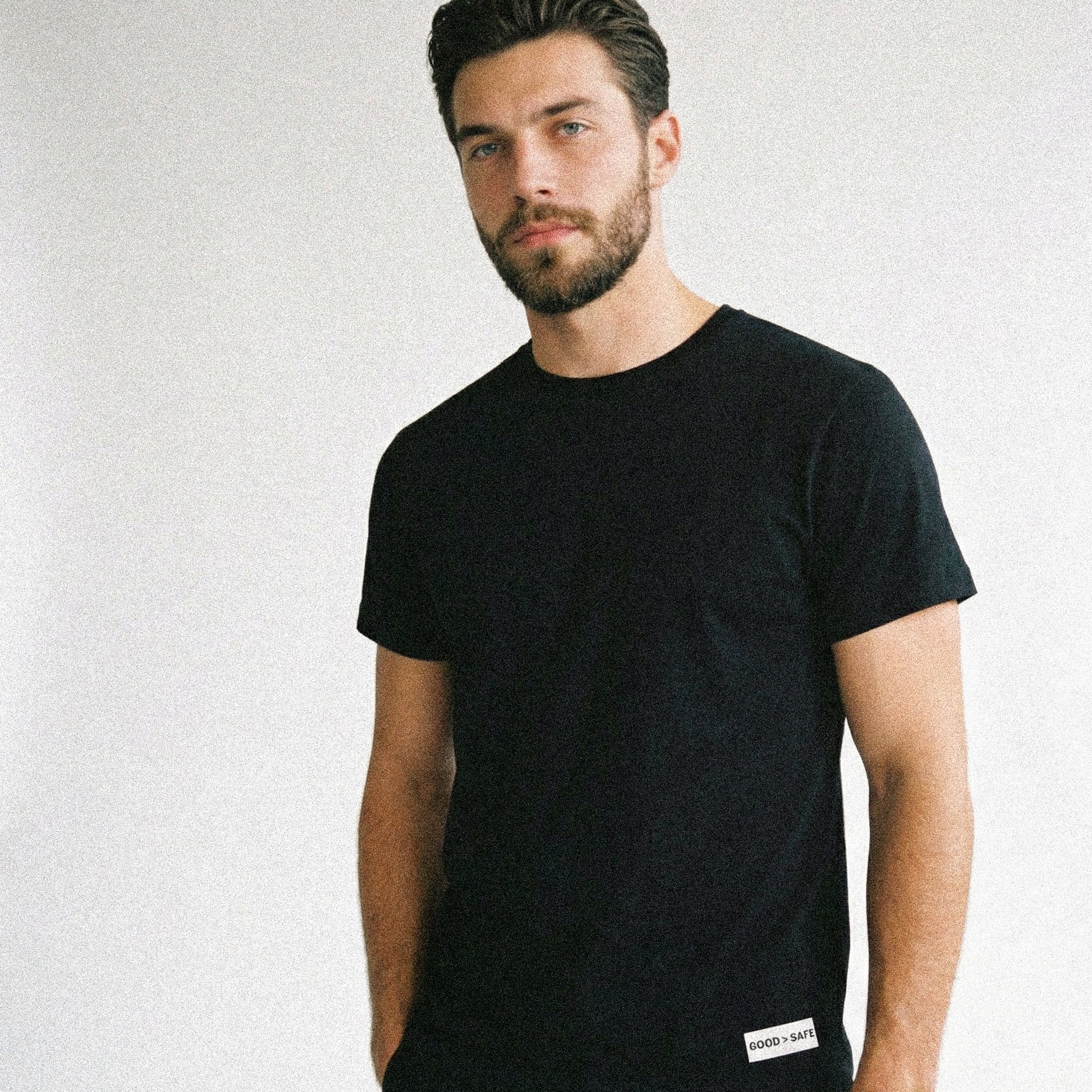Man wearing a black t-shirt with a brand logo on a light gray background