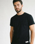 Man wearing a black t-shirt with a brand logo on a light gray background