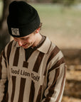Person wearing a striped sweater with 'Good Lion Golf' text and a black beanie outdoors.