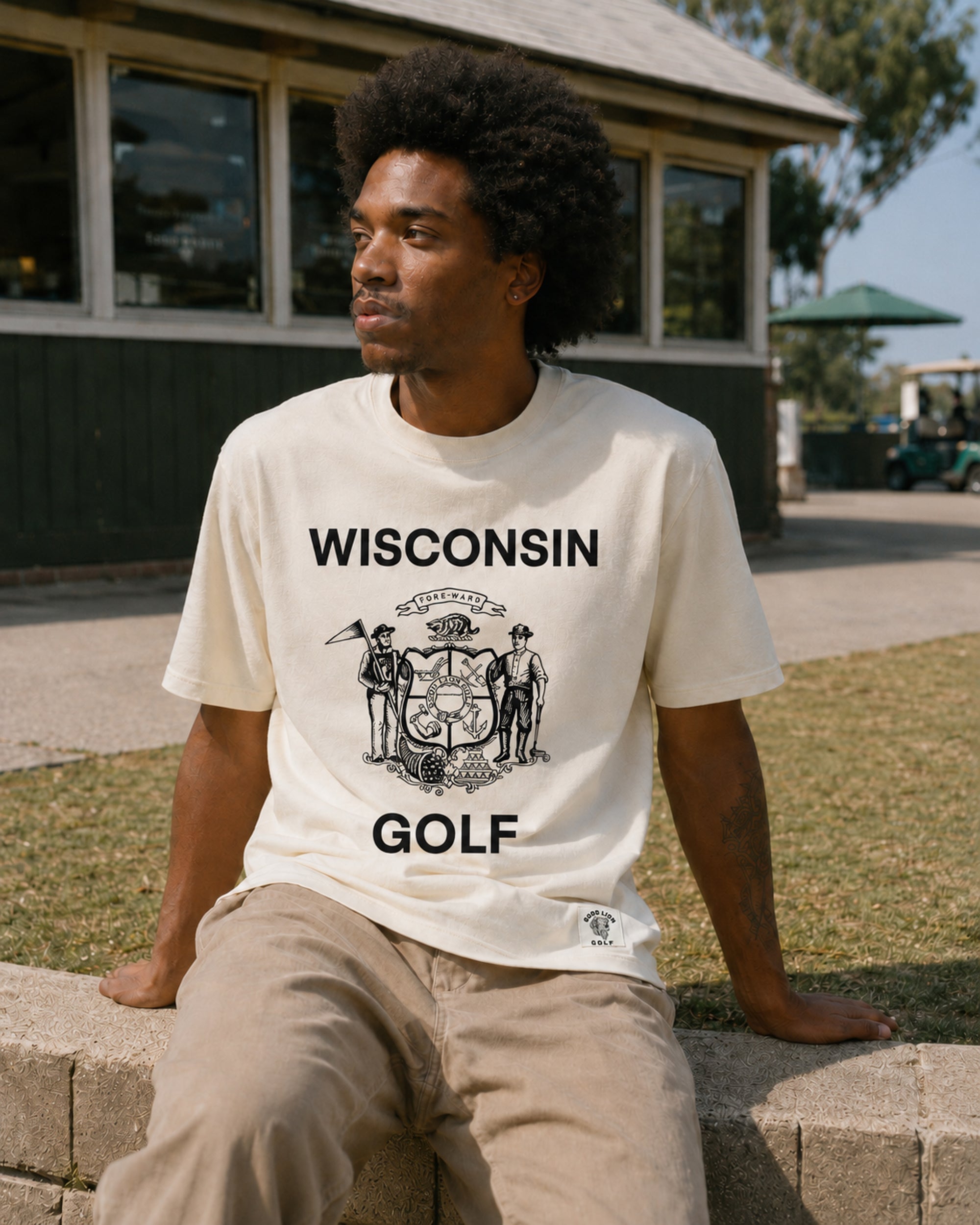 Person wearing a 'Wisconsin Golf' t-shirt sitting outdoors.
