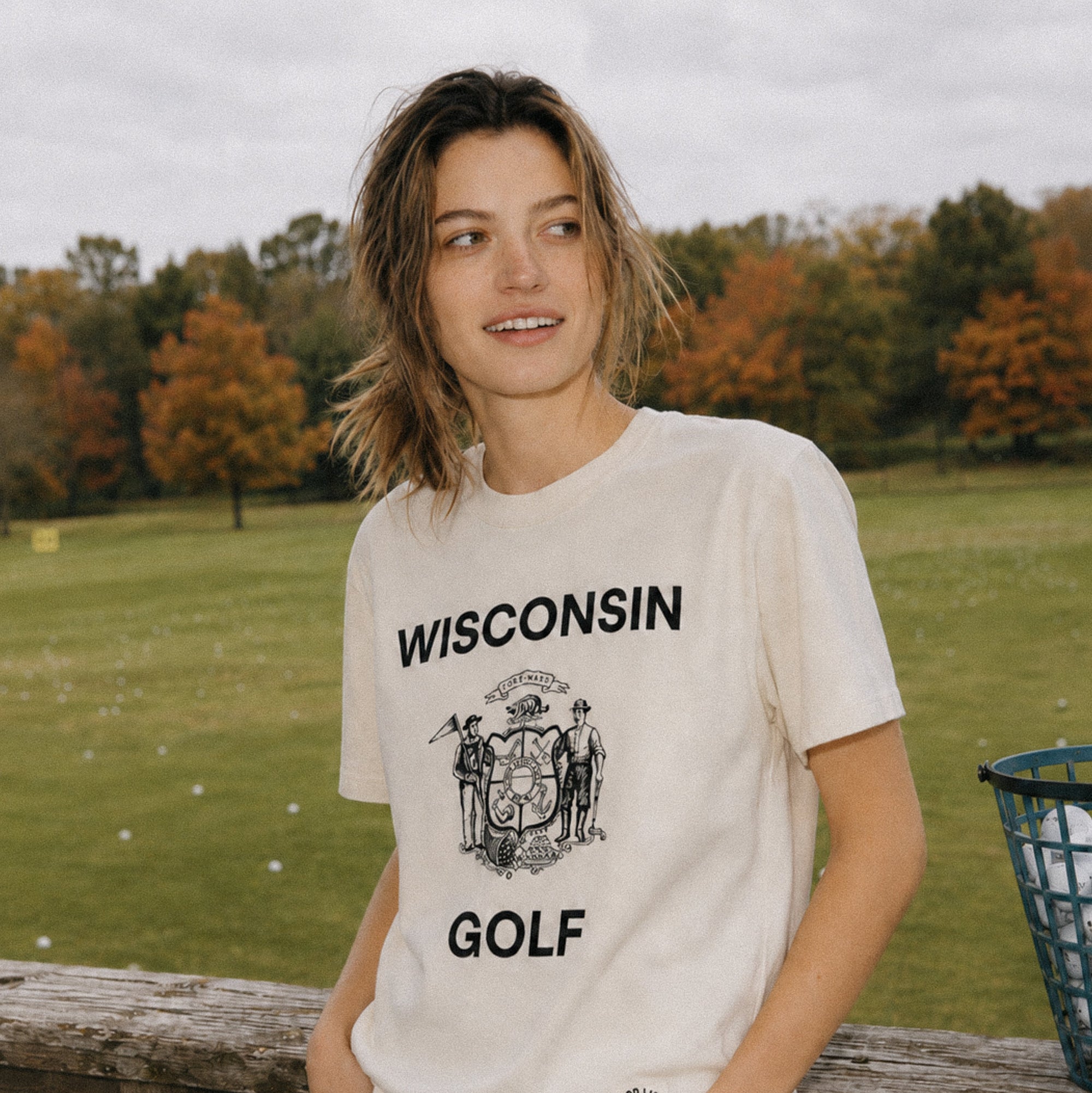 Person wearing a 'Wisconsin Golf' t-shirt standing outdoors with trees and grass in the background